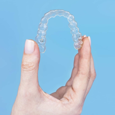Invisalign Comprehensive 7 Woman holding invisible transparent aligner invisalign or plastic orthodontic braces, clear-plastic retainer on blue background