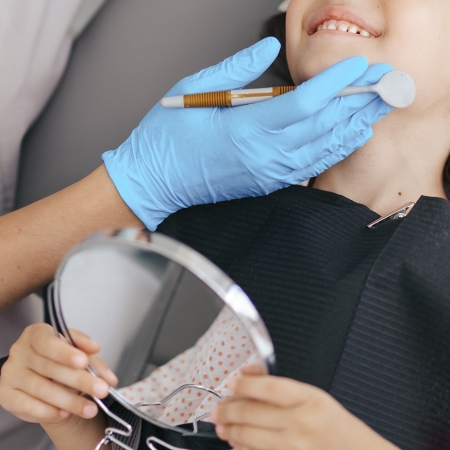 Invisalign First 8 Cute little girl sitting on a modern dental chair and having dental consultation with dentist