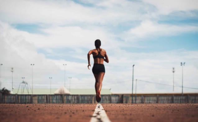 rear-view-female-athlete-running-track-field-against-sky